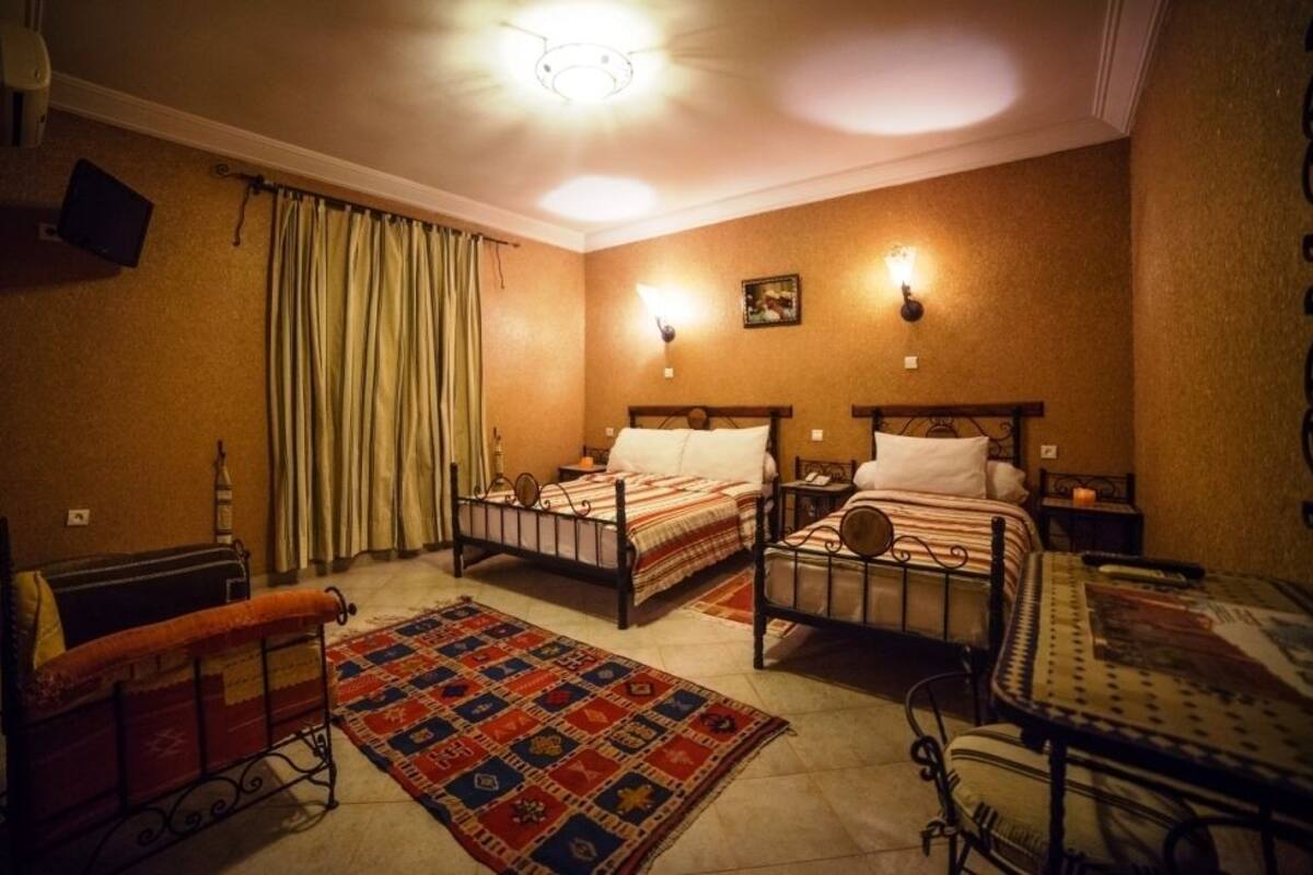 Una habitación con dos camas, una mesita, un banco y una alfombra estampada.