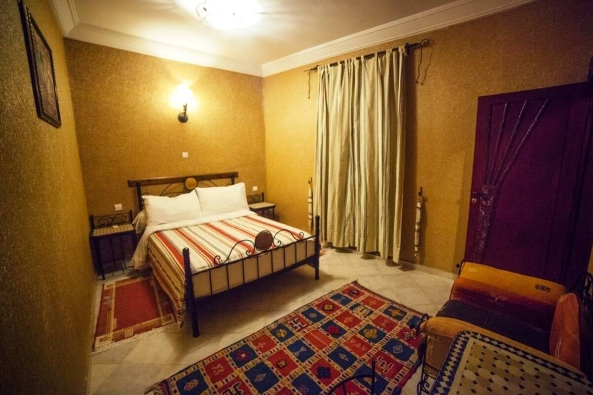 Un dormitorio con cama, mesitas de noche, alfombra, una silla y una puerta.