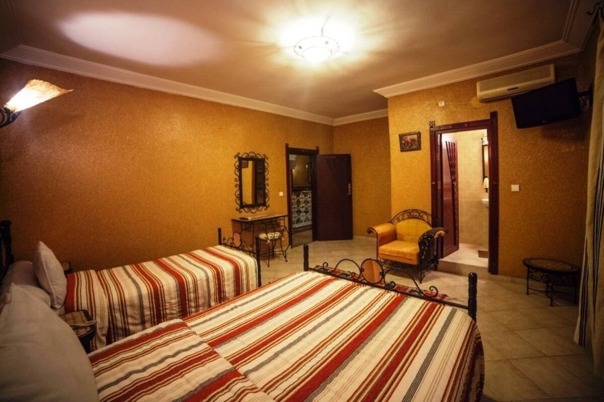 Habitación de hotel con dos camas, una silla, una mesa y un televisor.