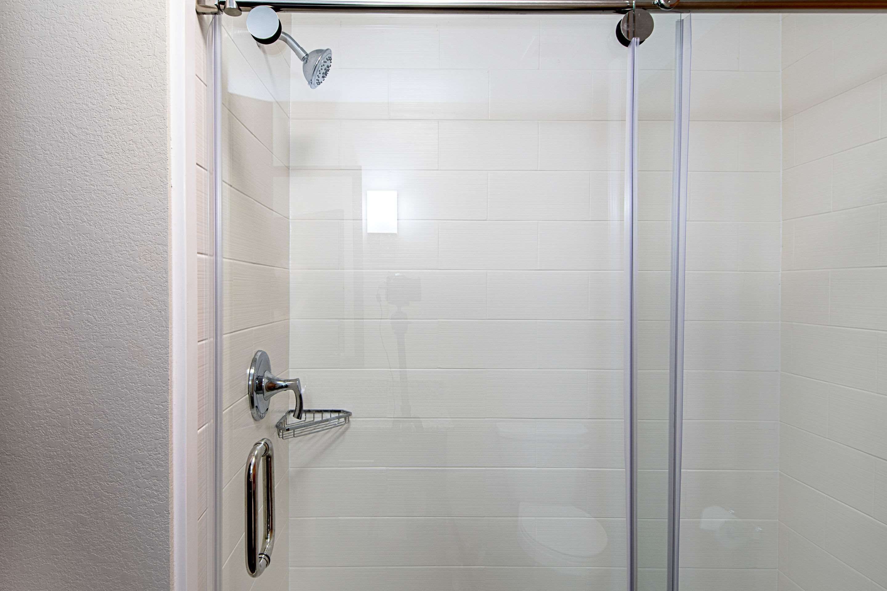 A glass-enclosed shower with a handheld showerhead and a wall-mounted faucet.