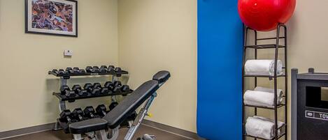 A gym with a bench, dumbbells, a red exercise ball, and towels on shelves.