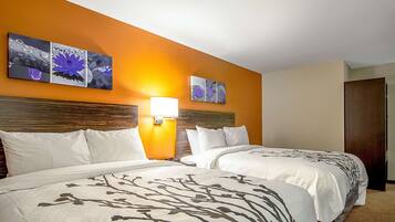 A hotel room with two beds, a nightstand, a lamp, and artwork on the wall.