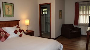 A hotel room with a bed, a chair, a nightstand, a lamp, and a mirror. - Pousada Chablis (Campos do Jordão)