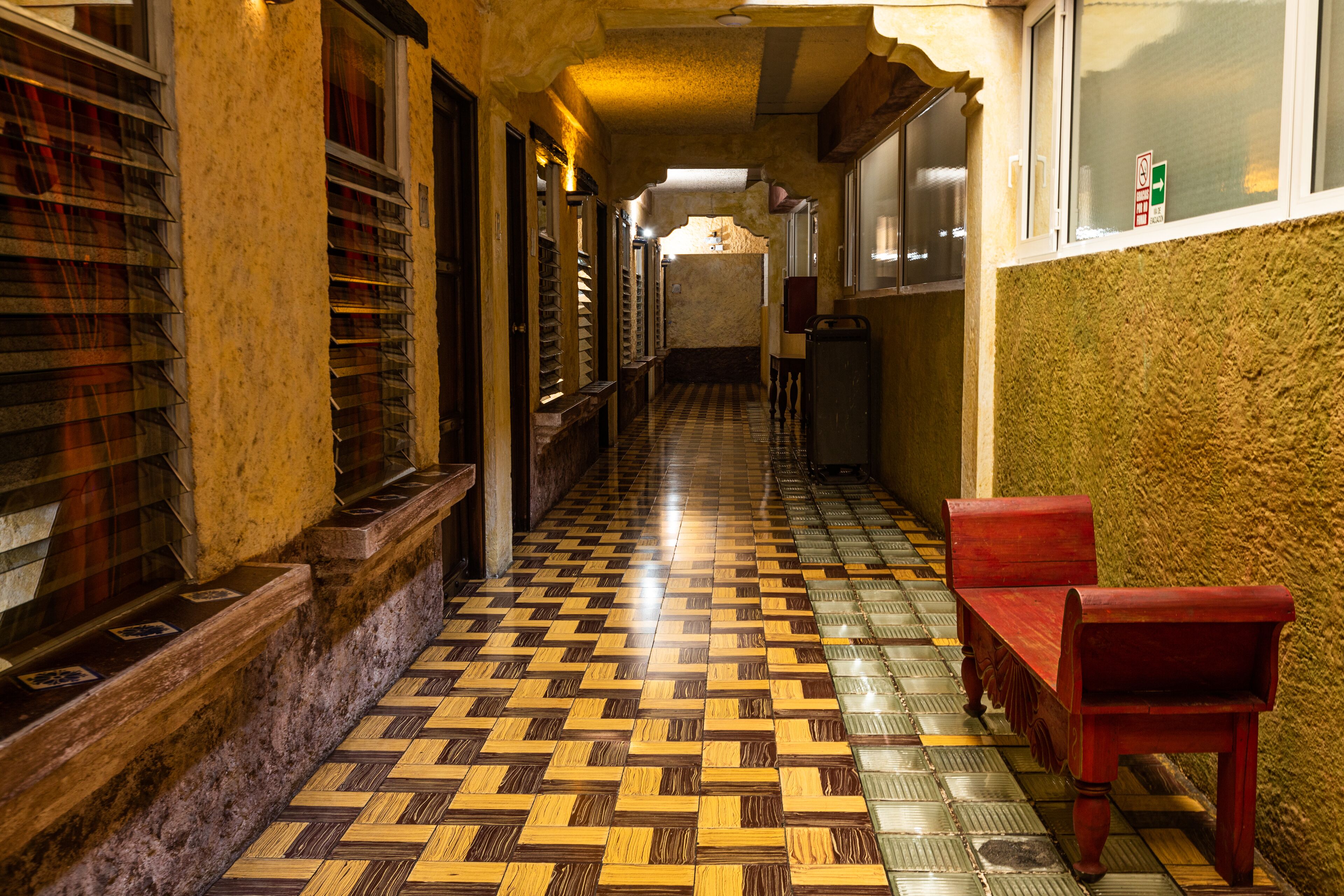 A hallway with patterned flooring, a bench, and a window with a sign.