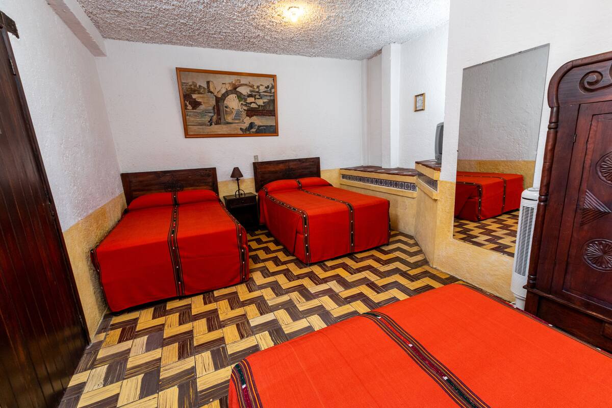A room with three beds, a wooden wardrobe, a painting on the wall, and a patterned floor.