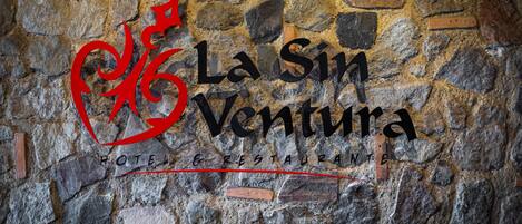 Un mur de pierre sur lequel est inscrit le texte « La Sin Ventura Hotel Restaurante » et un logo rouge.