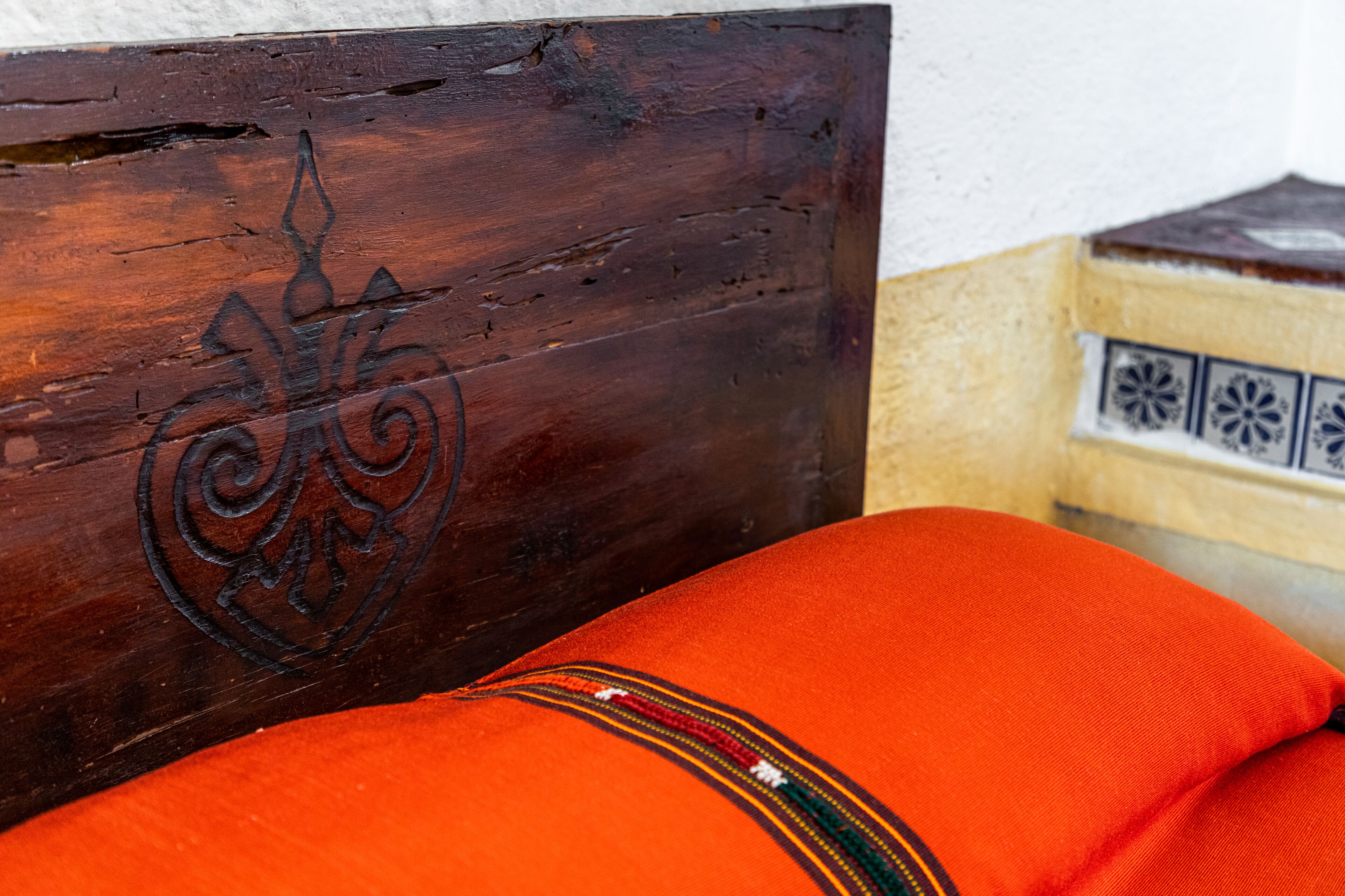 A wooden headboard with a carved design, a red cushion, and a tiled wall in the background.