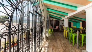 Ein Balkon mit schmiedeeisernem Geländer, Holzboden und grünen und gelben Stühlen.