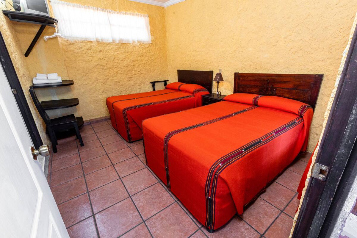 A room with two beds, a small table, a chair, and a window with a curtain.