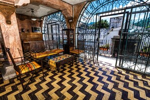 A room with a checkered floor, a wooden bench with colorful cushions, and a television on a wooden cabinet. - Hotel La Sin Ventura (Antigua Guatemala)