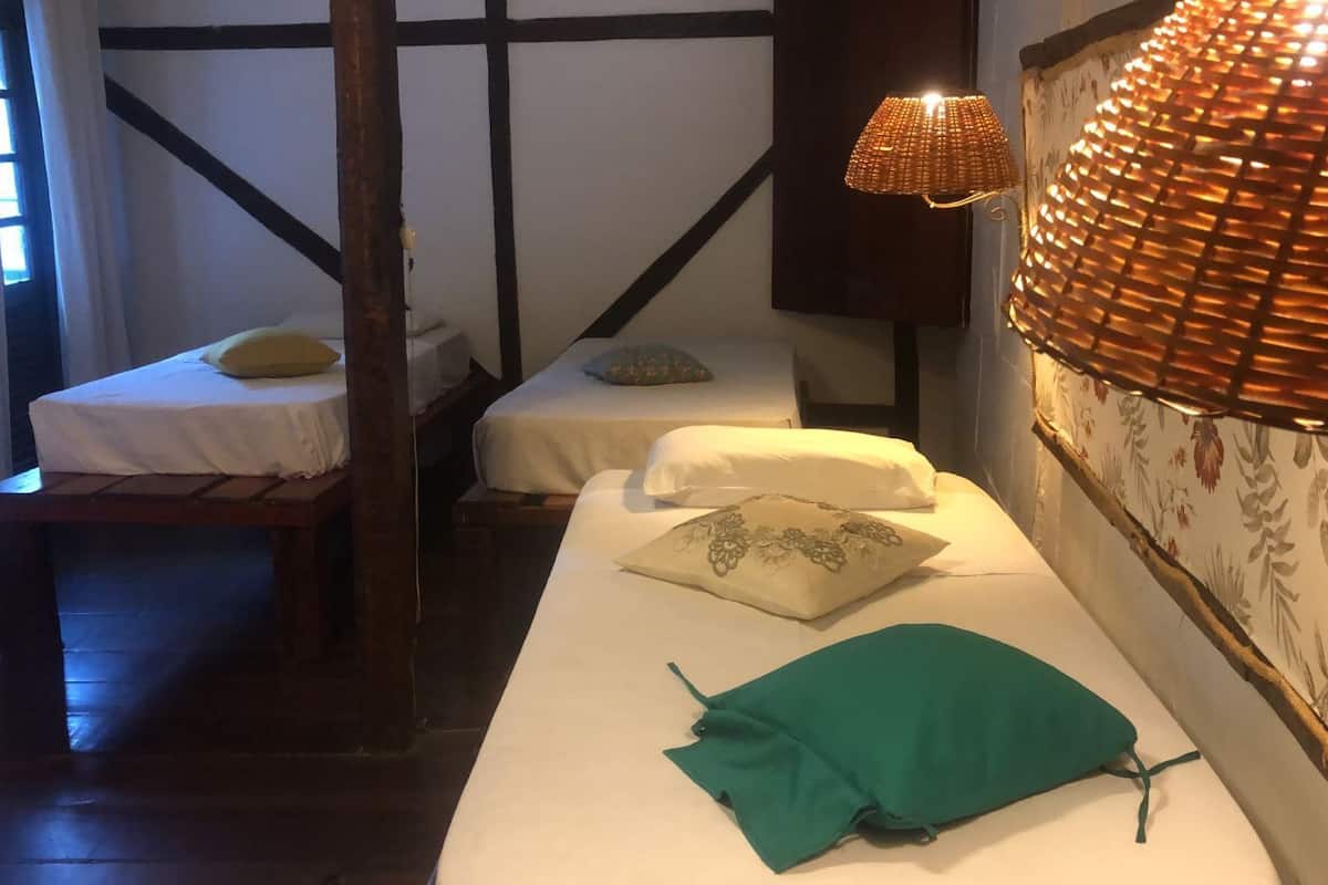 A room with two single beds, a bench, a lamp, and a floral wallpaper.