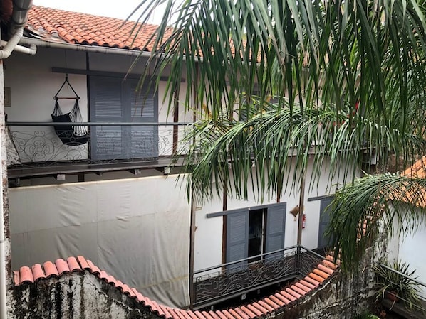 Un edificio de dos pisos con techo de tejas, un balcón con barandal de metal y una hamaca colgada.