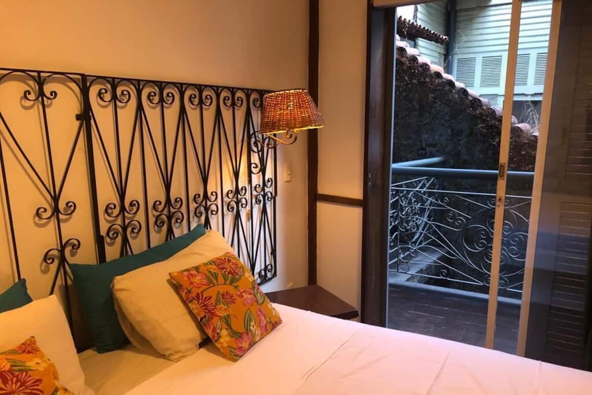 A bedroom with a bed, pillows, a decorative metal headboard, and a view of a balcony with a railing.