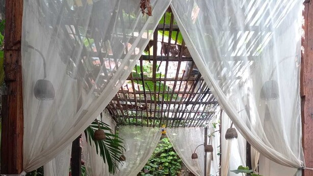 An outdoor patio area with a wooden pergola, white drapes, and wicker furniture. - Palma Hostel (São Luís)