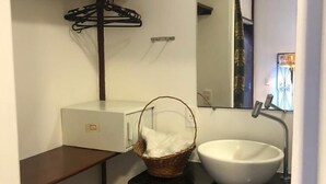 A bathroom with a white sink, a mirror, a wooden shelf, and a basket. - Palma Hostel (São Luís)