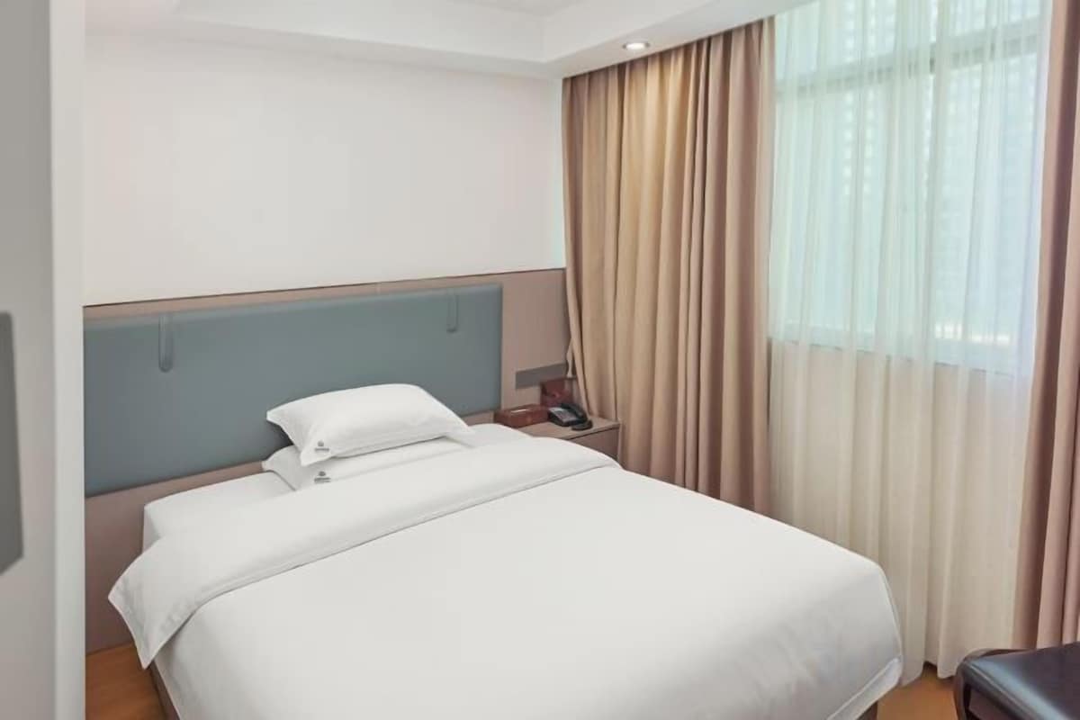 A hotel room with a bed, a nightstand, a lamp, and a window with curtains.