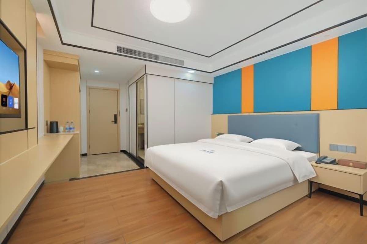 A hotel room with a bed, bedside table, and a TV mounted on the wall.