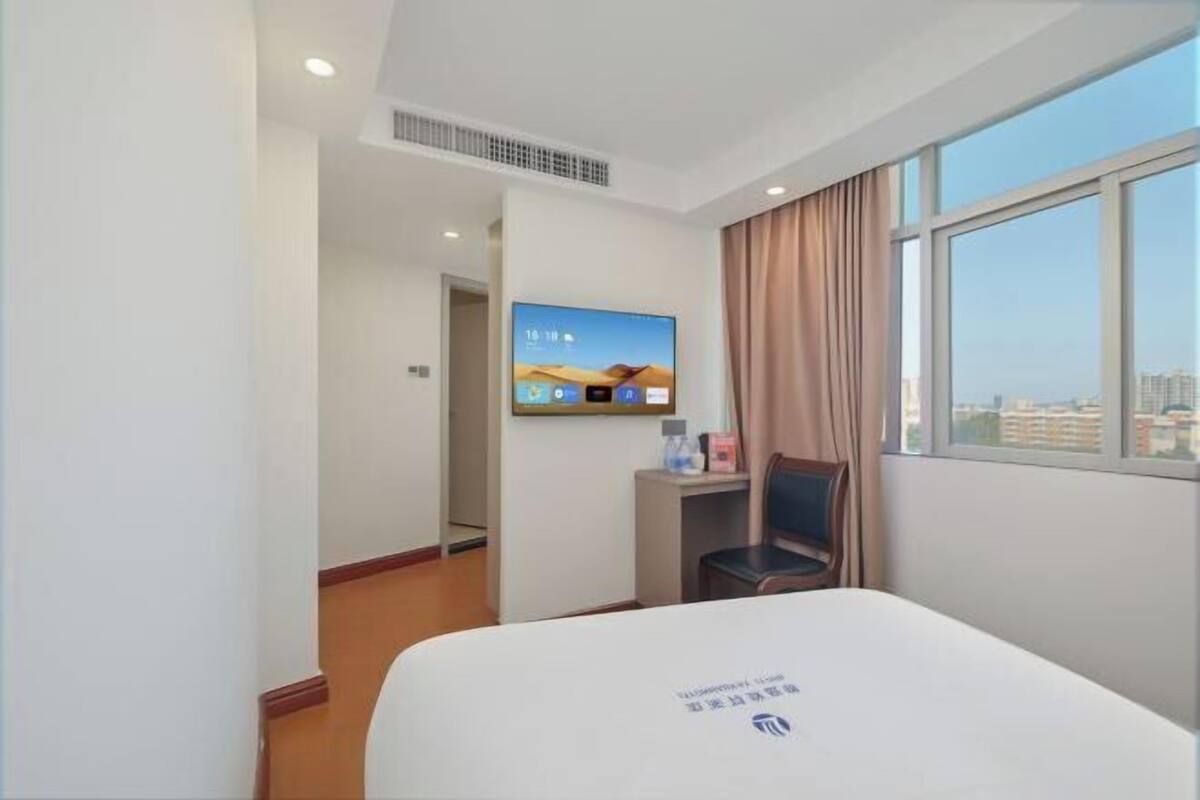 Una habitación de hotel con cama, televisión montada en la pared, escritorio y silla.