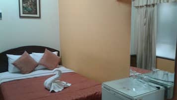 A hotel room with a bed, pillows, a fan, a small table, and a mirror.