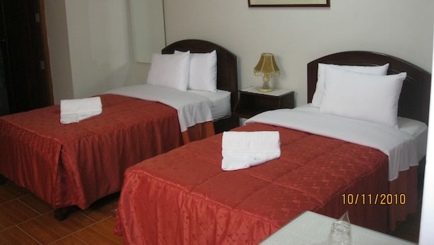 A hotel room with two beds, each with a red bedspread and white pillows, a nightstand with a lamp, and a painting on the wall. - Hotel Plaza Bolognesi (Trujillo)