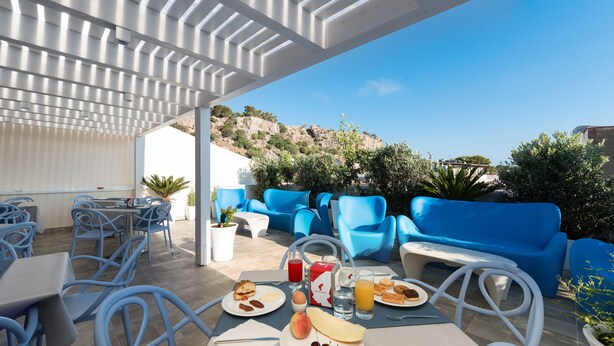 An outdoor dining area with blue chairs and tables, a breakfast spread, and a view of a hillside.