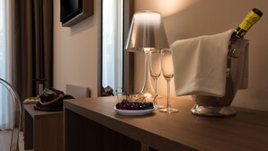 A hotel room with a wooden table, a plate of cherries, two champagne flutes, a lamp, and a bottle of champagne.