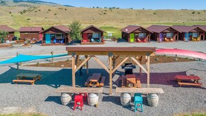 Un camping con varias cabañas, mesas de picnic y parrillas.