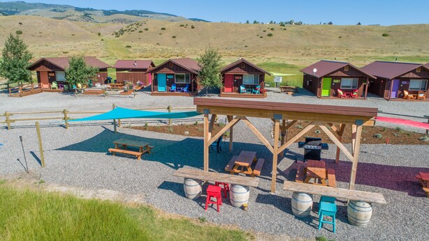 Un camping con varias cabañas, mesas de picnic y una zona de estar cubierta.