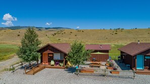 Un alojamiento de estilo rústico tipo cabaña, con patio de grava, mesas de picnic y vistas panorámicas a una colina.