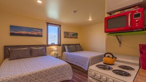 Una habitación compacta con dos camas, una kitchenette con estufa y microondas, y un ventanal con vistas.