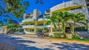 A multi-story hotel with a stone facade, balconies, and parked cars. - Meridian 202 by PRP (Playa del Carmen)