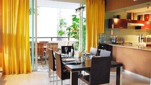 A modern living room with a dining area, featuring a large window, yellow curtains, a dining table with chairs, and a kitchen area with cabinets and appliances. - Meridian 202 by PRP (Playa del Carmen)