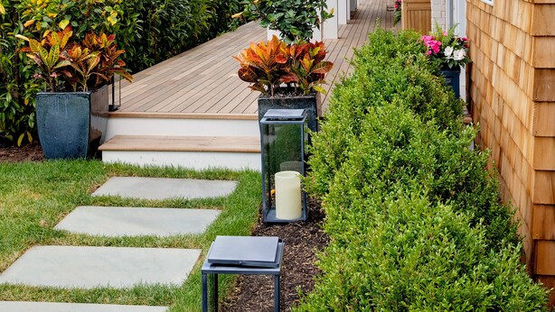 A modern building with a wooden exterior, a balcony, and a pathway lined with potted plants and stepping stones.