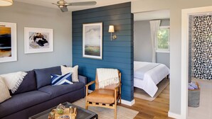 A modern room with a blue accent wall, a sofa, a chair, a bed, and a small table with decorative items.