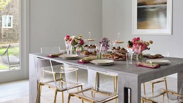 Un comedor con una mesa larga dispuesta para una comida, con sillas de vidrio transparente y una lámpara colgante moderna.