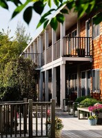 Un edificio de varios pisos con balcones, una terraza de madera y plantas en macetas.