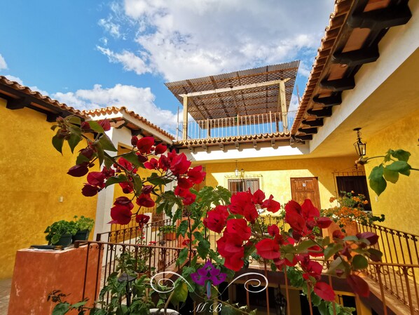 A courtyard with a yellow wall, a wooden balcony, and red flowers.