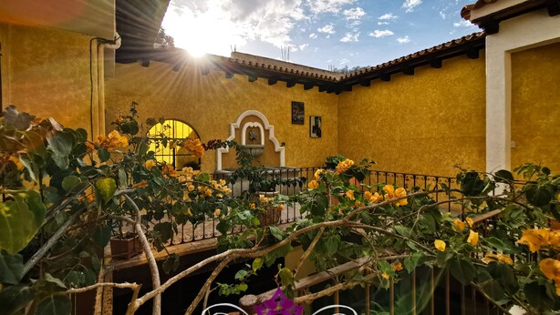 A courtyard with yellow walls, a fountain, and a view of the sky. - Maison Bougainvillea (Antigua Guatemala)
