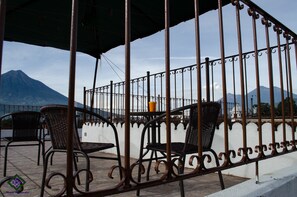A terrace with metal railings, wicker chairs, and a view of mountains.