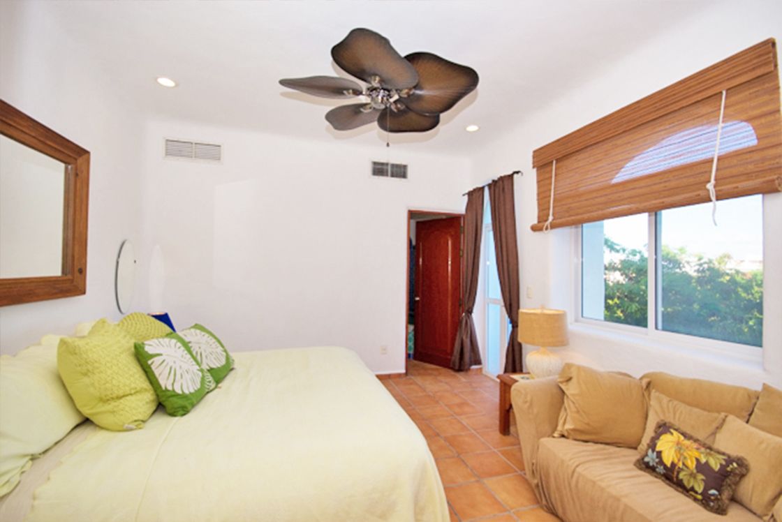 A bedroom with a bed, a ceiling fan, a window with curtains, and a sofa.