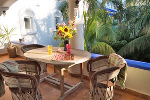 Une terrasse extérieure avec une table ronde en bois, des chaises en osier, un vase rempli de fleurs et une vue sur des palmiers.
