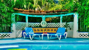 A pool area with a blue and yellow lounge chair set under a pergola, surrounded by lush greenery. - Natz Ti Ha A301 by PRP (Playa del Carmen)