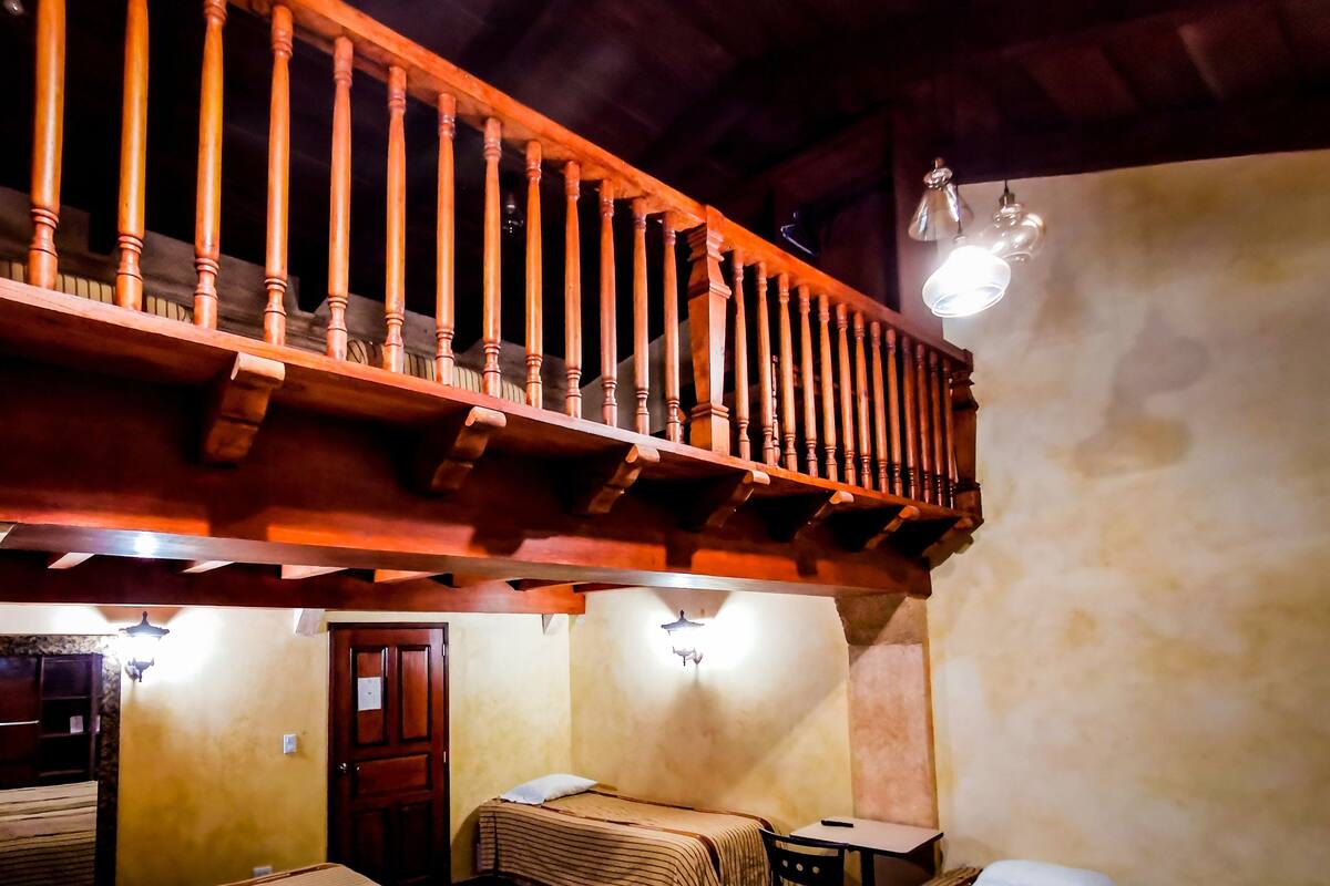 Una habitación con cuatro camas, un balcón de madera y una pequeña mesa.