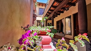 Une cour agrémentée de plantes et de fleurs en pot, une pergola en bois et un bâtiment doté d’un toit en tuiles.