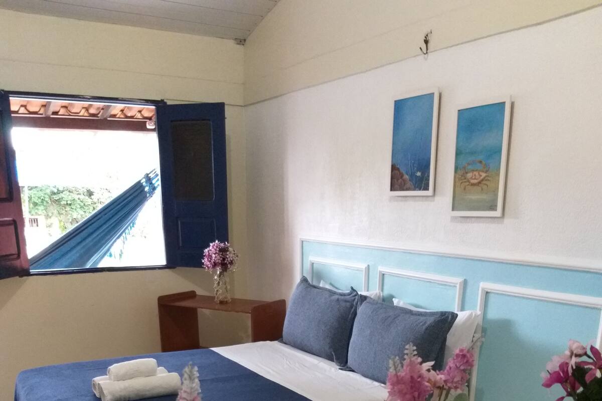 A bedroom with a bed, bedside tables, a nightstand, a window, and wall art.