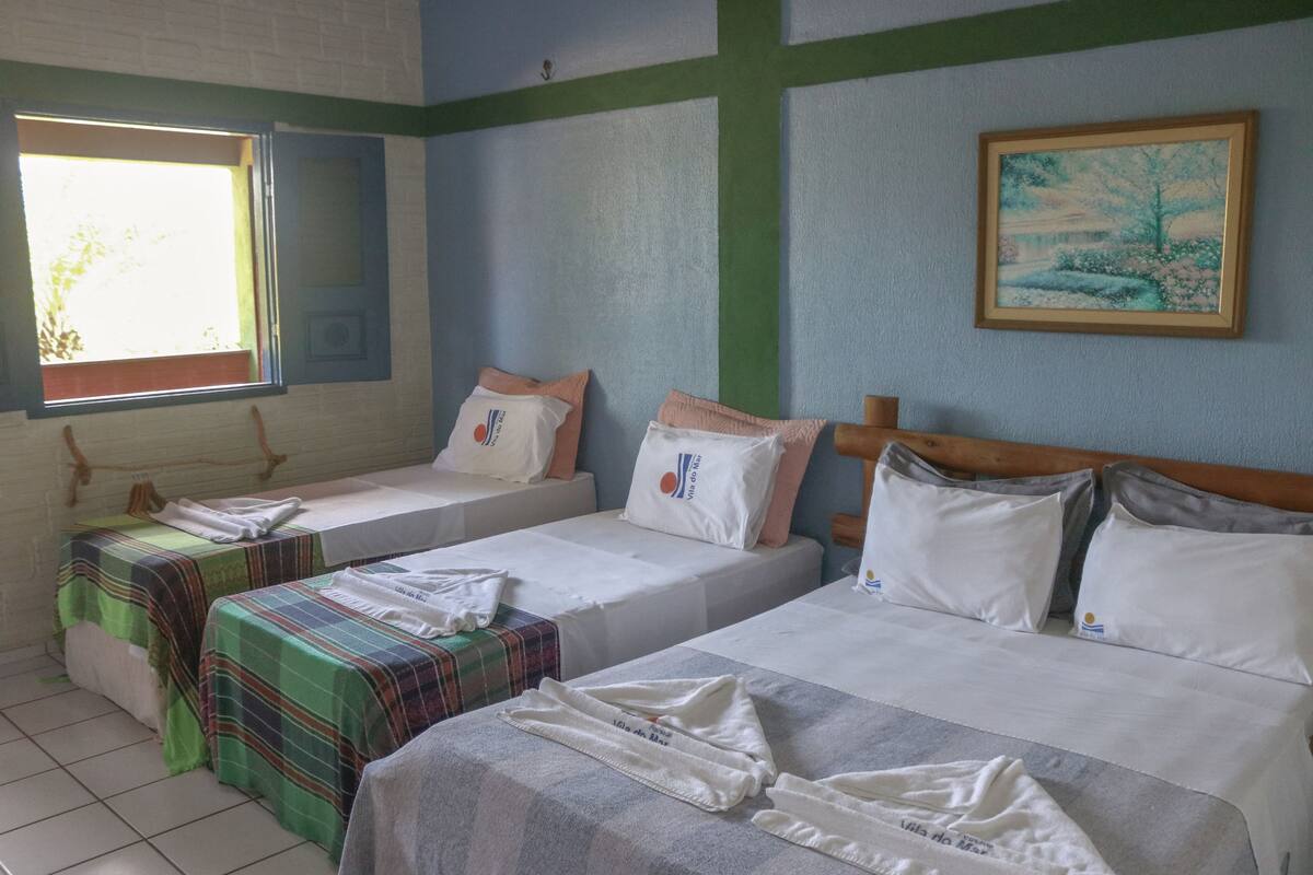 A hotel room with two single beds, a window with curtains, a painting on the wall, and a tiled floor.