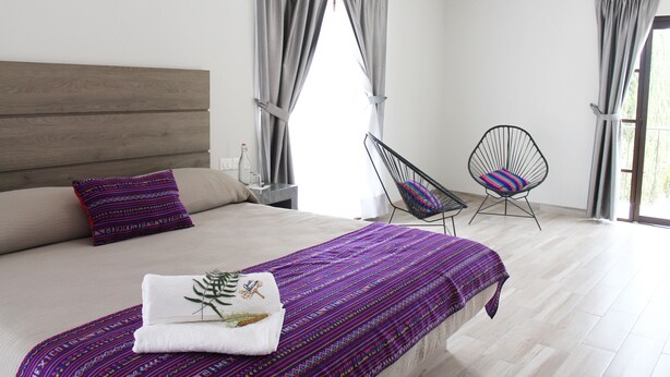 A bedroom with a bed, a chair, and a window with curtains. - Quinta Huizache (Nopaltepec)