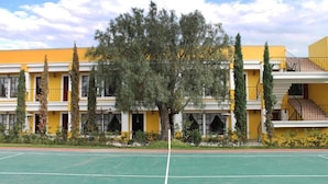A yellow building with a tennis court in front. - Quinta Huizache (Nopaltepec)