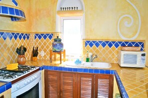 Una cocina con estufa a gas, microondas, lavabo y azulejos decorativos.