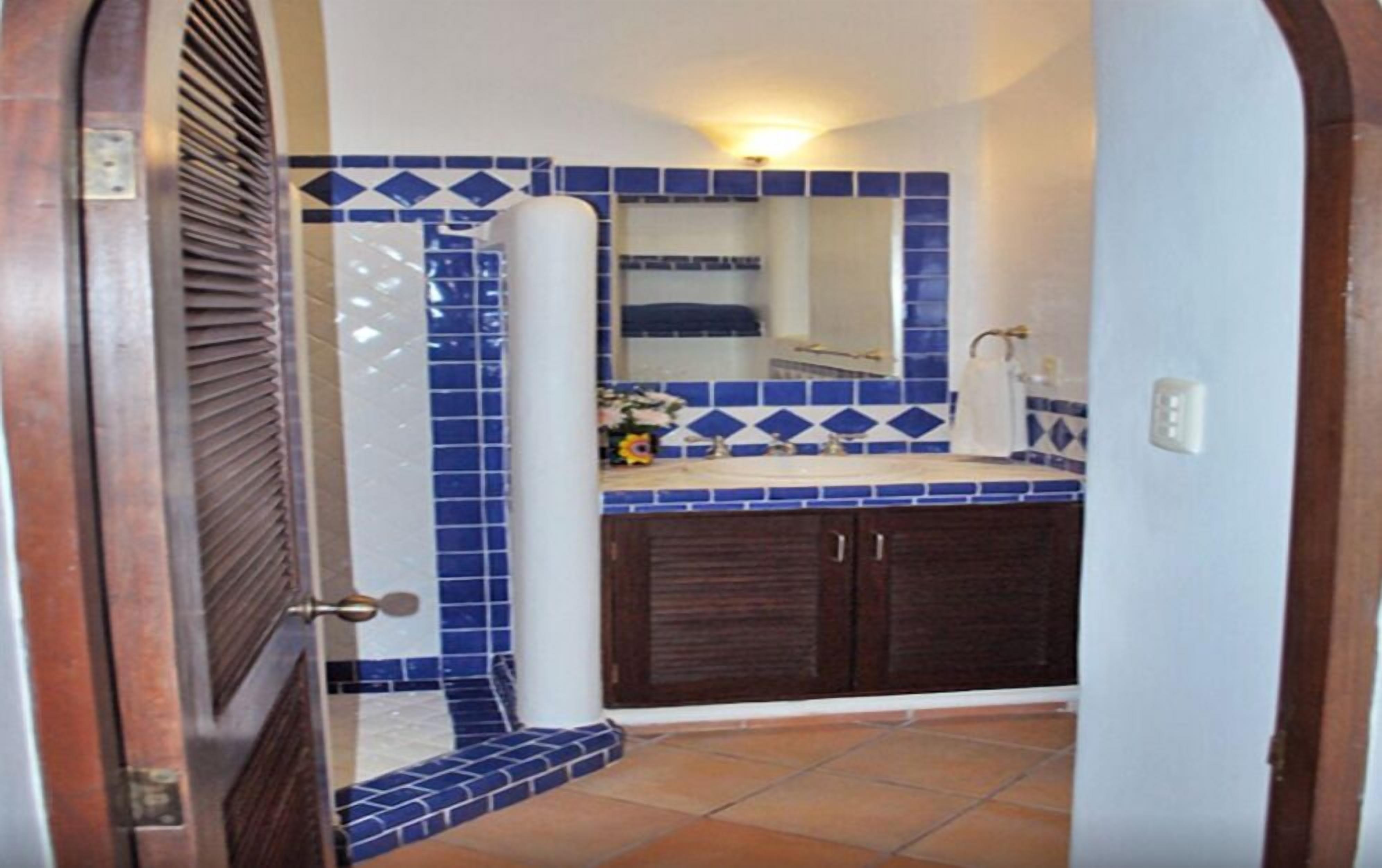 Casa de banho com azulejos azuis e brancos, pia, espelho e zona de duche.